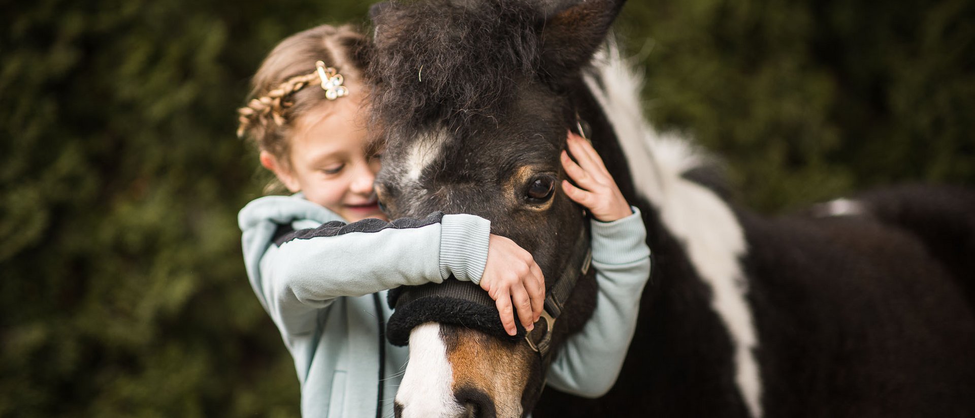 Der Ursprung des Wohlgefühls: Ihr Hotel im Pustertal Mädchen umarmt und hält ein schwarzes Pony mit weißem Abzeichen