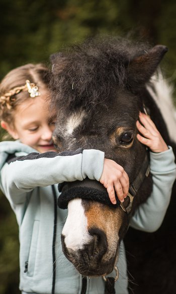 Ihre Hotels in Südtirol: die Heimat der Fülle Mädchen umarmt und hält ein schwarzes Pony mit weißem Abzeichen