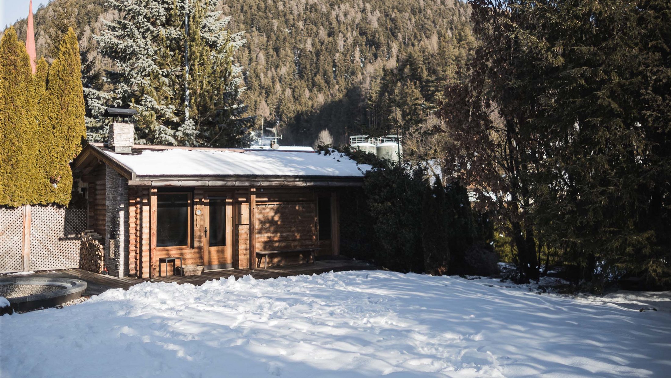 Der Ursprung des Wohlgefühls: Ihr Hotel im Pustertal Holzhaus mit schneebedecktem Dach und Garten vor bewaldetem Hügel
