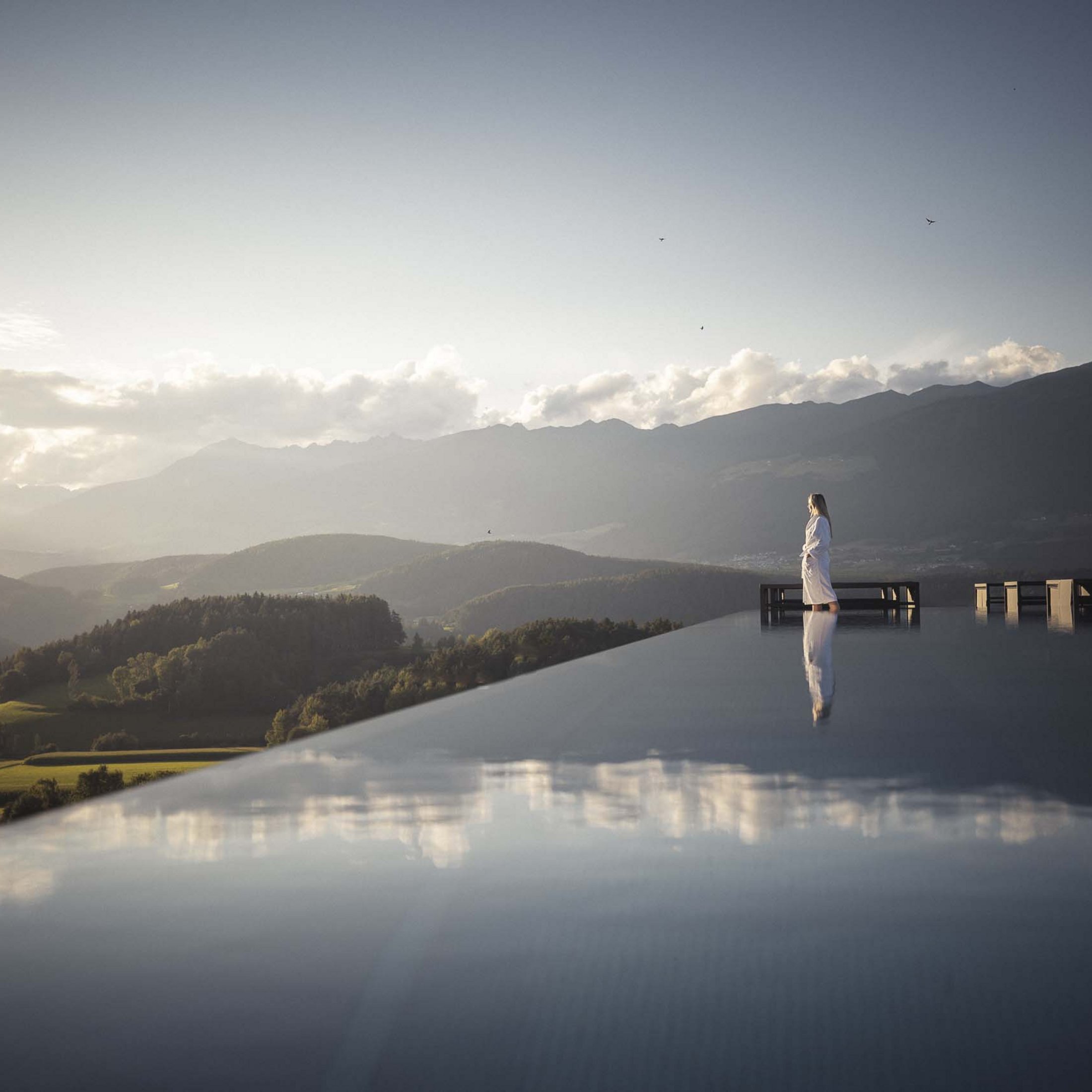 Ihre Hotels in Südtirol: die Heimat der Fülle Frau im Bademantel steht am Rand eines Infinity-Pools mit Bergpanorama