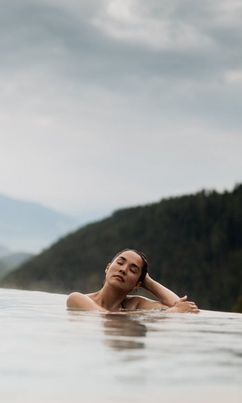 Ihre Hotels in Südtirol: die Heimat der Fülle Frau entspannt in Infinity-Pool mit Bergblick und bewölktem Himmel