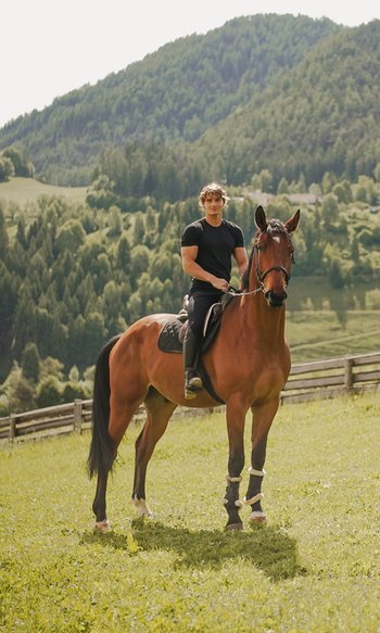 Ihre Hotels in Südtirol: die Heimat der Fülle Mann reitet braunes Pferd auf einer Wiese mit Bergen im Hintergrund