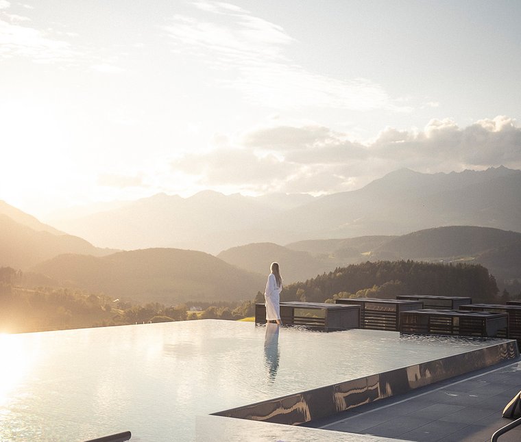 Ihre Hotels in Südtirol: die Heimat der Fülle Frau im Bademantel am Infinity-Pool mit Bergpanorama bei Sonnenuntergang