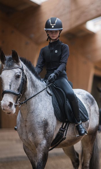 Ihre Hotels in Südtirol: die Heimat der Fülle Junge Reiterin auf grauem Pferd in Reithalle mit zweitem Reiter im Hintergrund