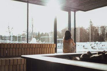 Wir sind Ihre Golfhotels in Südtirol. Frau in Sauna mit Blick auf verschneite Landschaft durch große Fenster