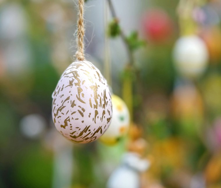 Ihre Hotels in Südtirol: die Heimat der Fülle Osterei mit goldenem Muster hängt an Faden vor unscharfem Hintergrund