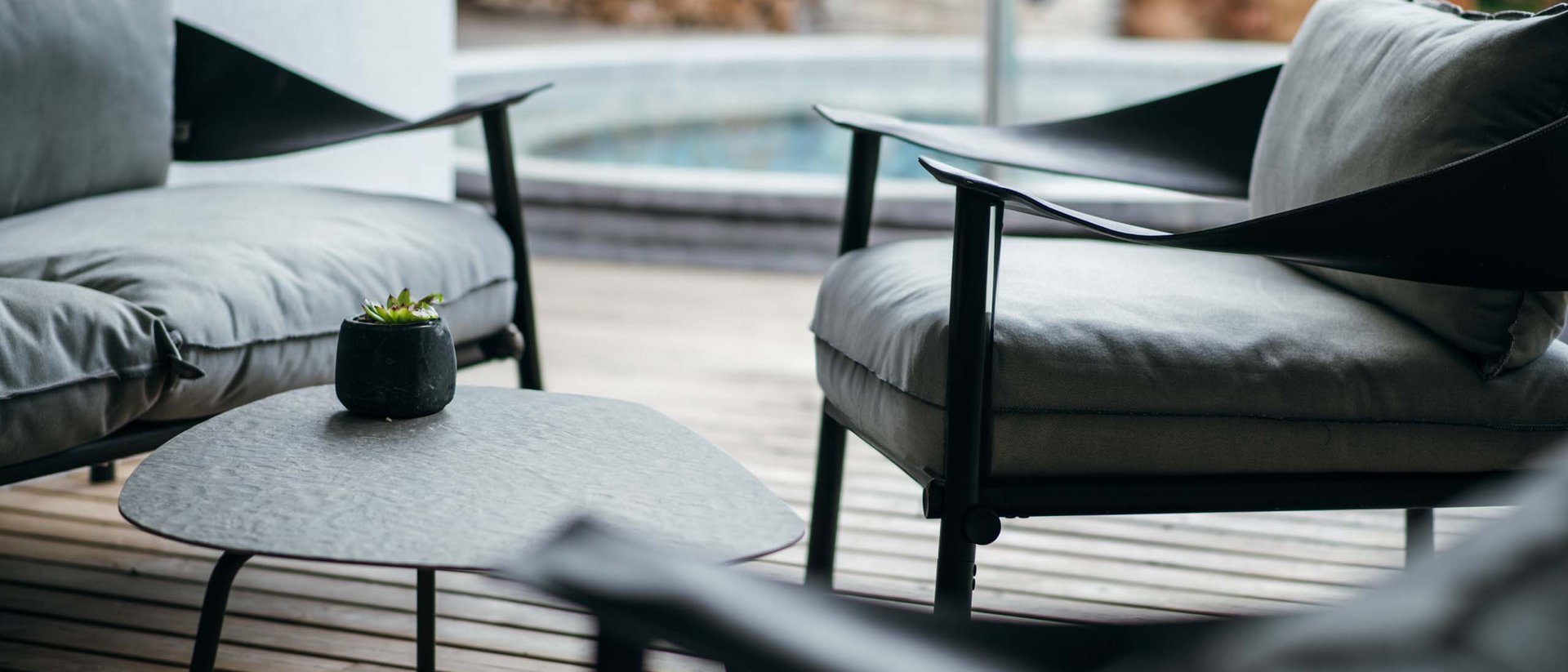 Der Ursprung des Wohlgefühls: Ihr Hotel im Pustertal Moderne Sitzgruppe mit grauen Polstersesseln und kleinem Tisch auf Holzterrasse