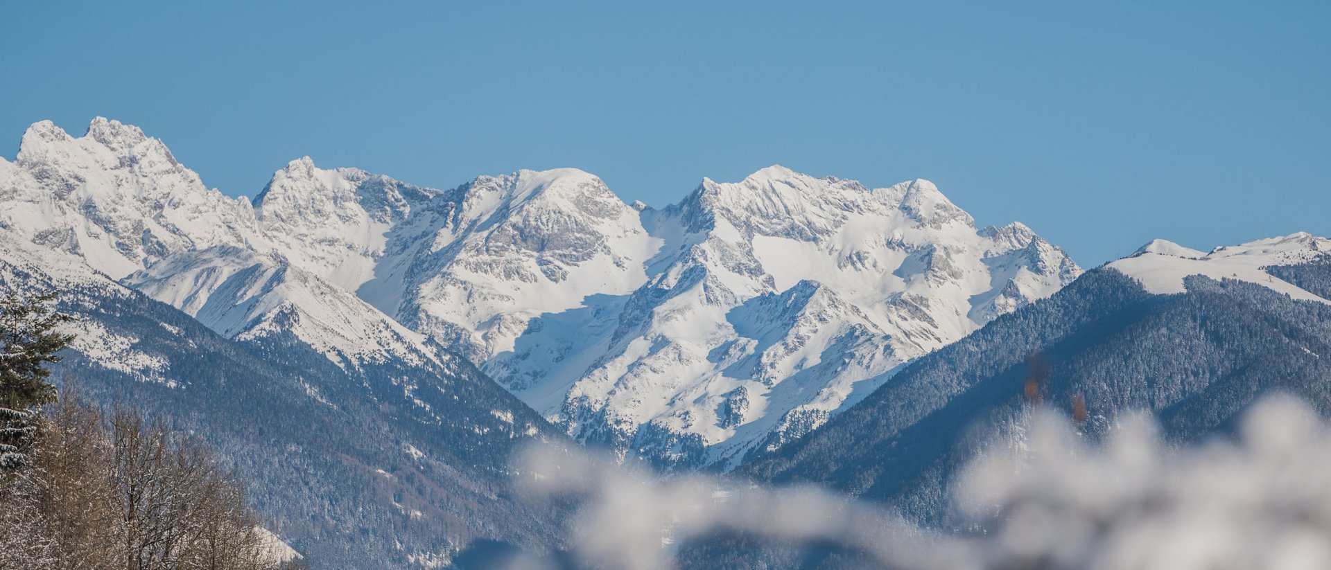 Der Ursprung des Wohlgefühls: Ihr Hotel im Pustertal Schneebedeckte Berge unter klarem Himmel mit verschneiten Bäumen im Vordergrund