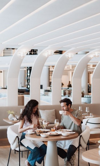 Ihre Hotels in Südtirol: die Heimat der Fülle Paar isst und trinkt in modernem Restaurant mit gebogenen weißen Deckenbögen