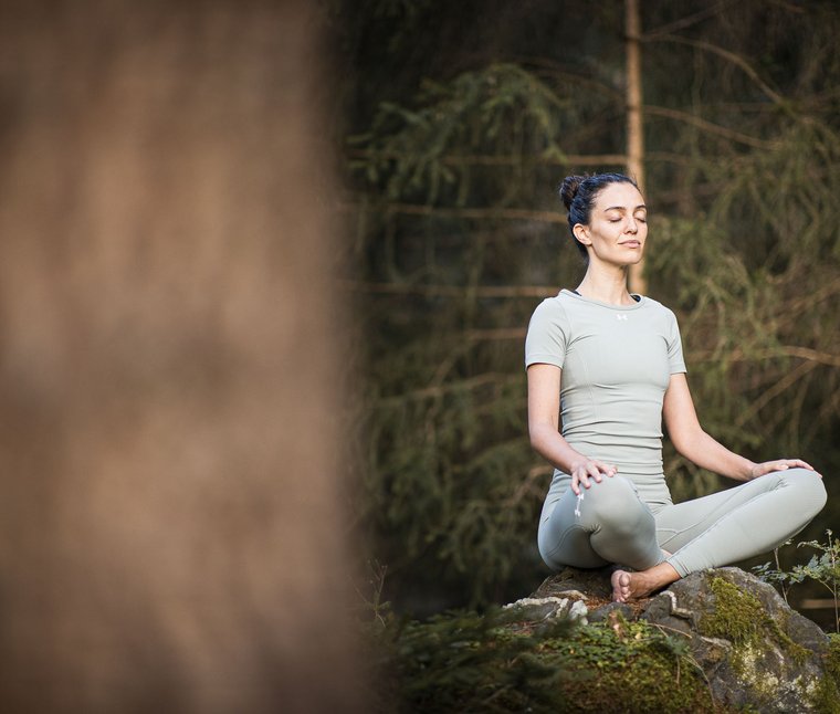 Ihre Hotels in Südtirol: die Heimat der Fülle Frau meditiert im Yoga-Sitz auf moosbedecktem Felsen im Wald