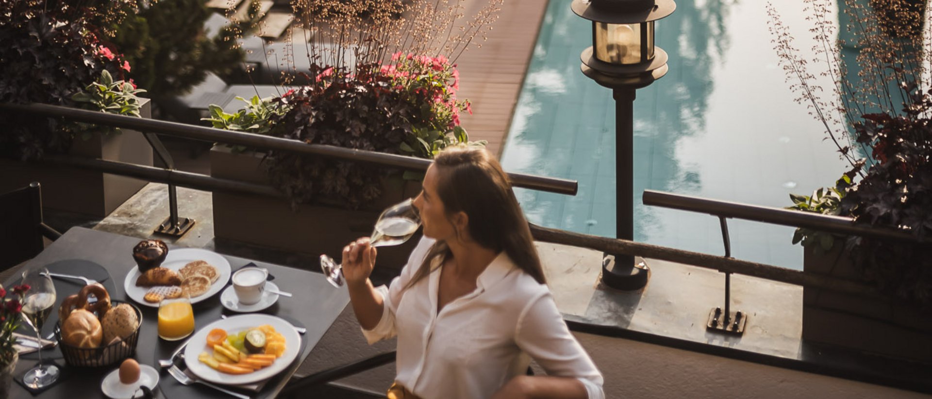 Der Ursprung des Wohlgefühls: Ihr Hotel im Pustertal Frau trinkt Wein beim Frühstück mit Pool und Bäumen im Hintergrund