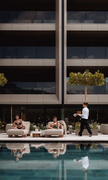 Ihre Hotels in Südtirol: die Heimat der Fülle Zwei Menschen entspannen auf Liegestühlen am Pool, Kellnerin bringt Getränke