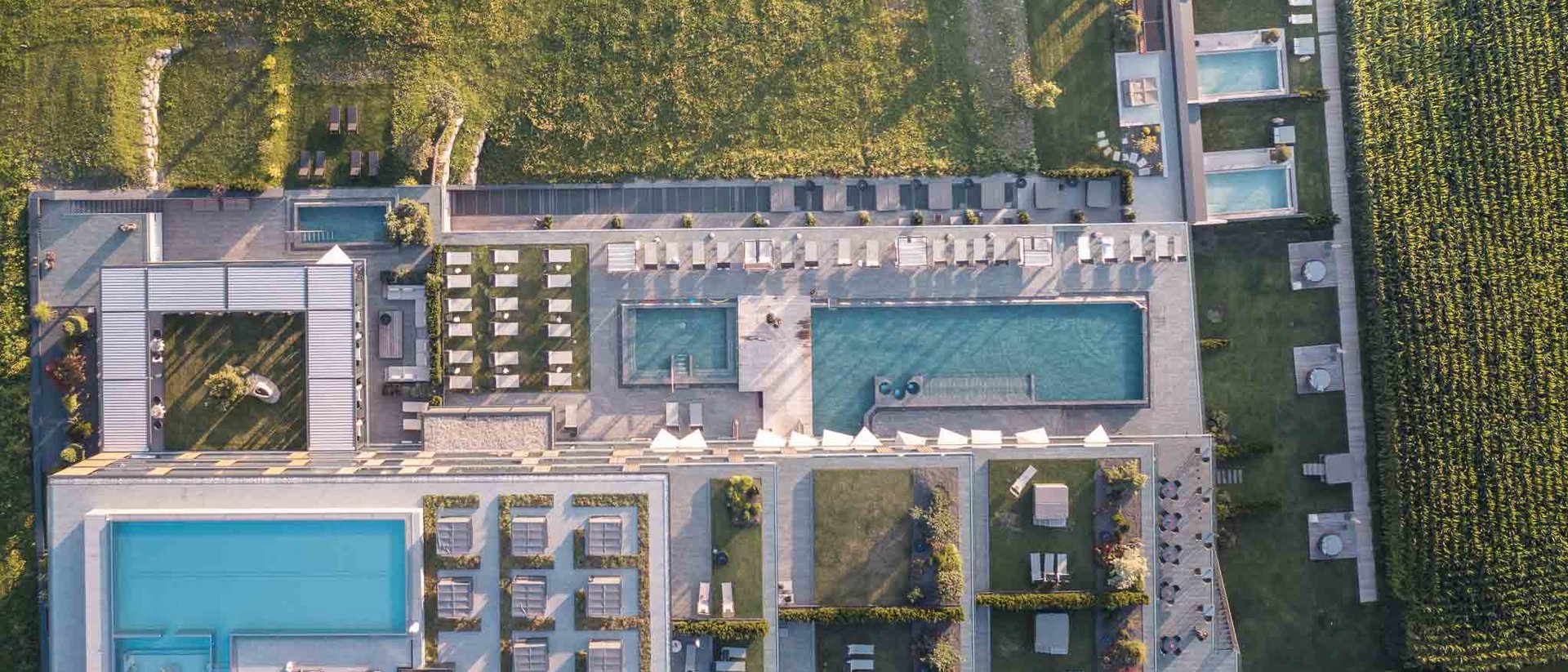 Die Quelle der Erfüllung: Ihr Hotel am Kronplatz Luftaufnahme einer Hotelanlage mit mehreren Pools, Liegestühlen und angrenzenden Feldern