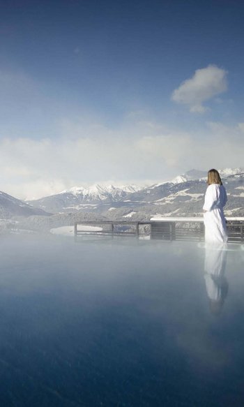 Ihre Hotels in Südtirol: die Heimat der Fülle Frau in Bademantel am beheizten Außenpool mit Blick auf schneebedeckte Berge