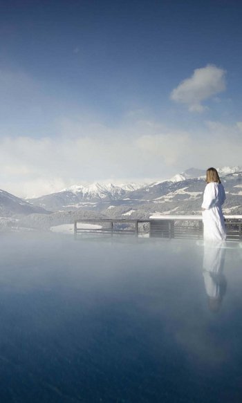 Ihre Hotels in Südtirol: die Heimat der Fülle Frau in Bademantel am beheizten Außenpool mit Blick auf schneebedeckte Berge