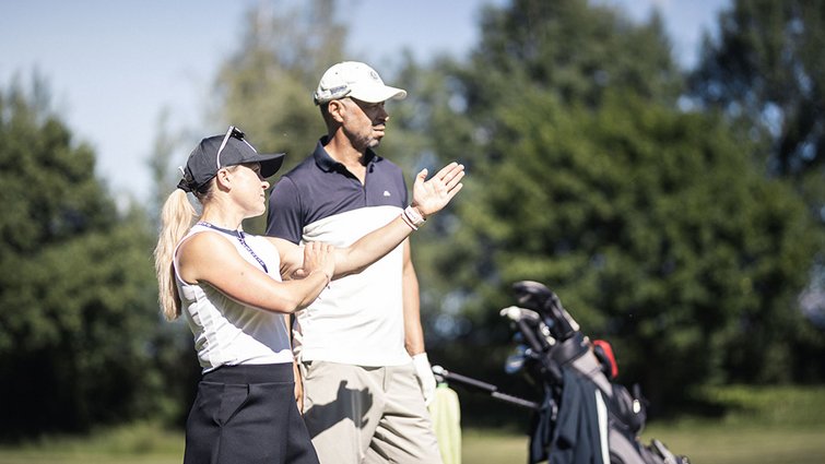 Wir sind Ihre Golfhotels in Südtirol. Zwei Golfer auf dem Golfplatz beim Gespräch, Golftasche im Hintergrund
