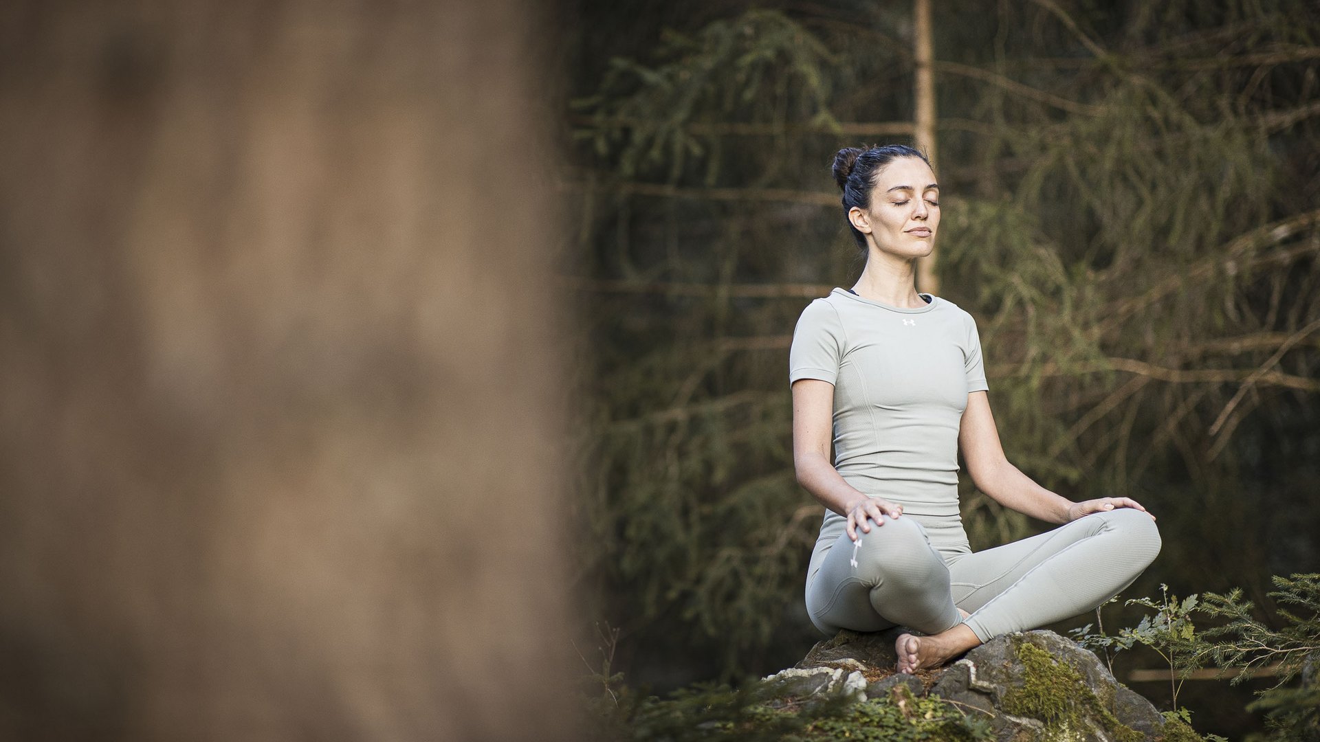 Ihre Hotels in Südtirol: die Heimat der Fülle Frau meditiert im grünen Wald sitzend auf einem Felsen